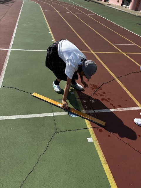 長い木の定規で地面のへこみを確認しています。